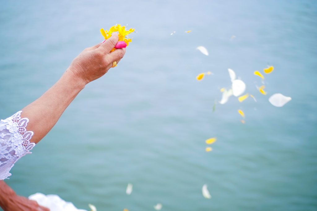 散骨セレモニーで花びらを海に撒く老婆の手